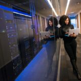 A woman using a laptop navigating a contemporary data center with mirrored servers.