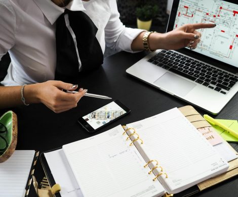 A business professional working on real estate project plans using multiple devices in an office setting.
